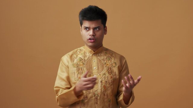 Positive Indian man in national cloth counting on fingers in the orange studio