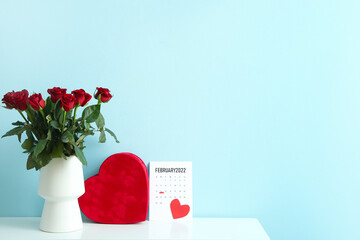 Bouquet of flowers, calendar with marked date of Valentine's Day and gift on table against color background