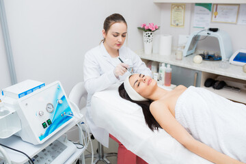 doctor-cosmetologist makes the procedure Microdermabrasion of the facial skin of a beautiful,...