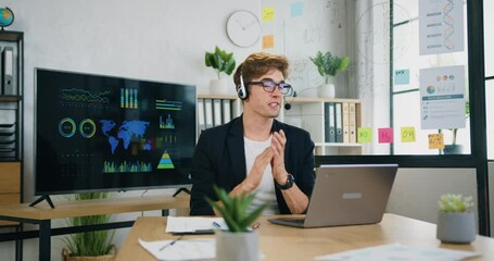 Smart caucasian guy using headphones video call communicate with business colleague friend from office room during brainstorming clapping hands