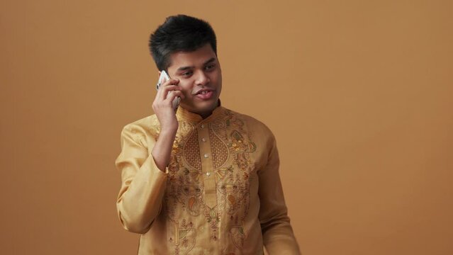 Positive Indian man in national cloth talking by phone in the orange studio