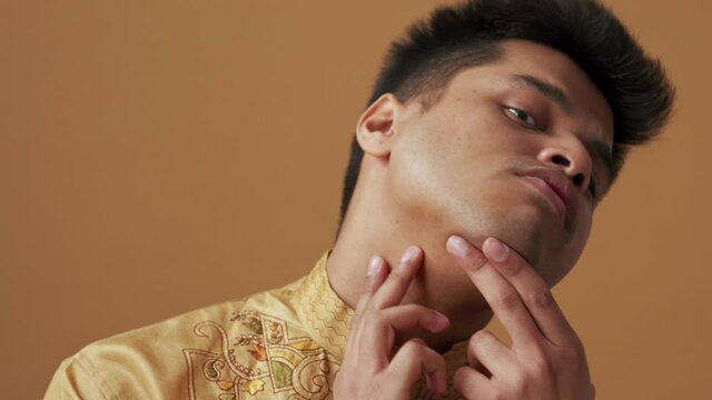 Handsome Indian man in national cloth looking at his skin at the camera in the orange studio
