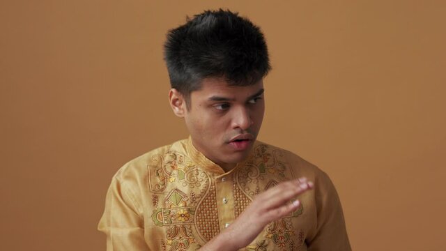 Confident Indian man in national cloth showing silence gesture in the orange studio