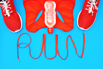 Running shoes and a tank with the lettering RUN made from a shoelace on a blue background. Creative active lifestyle concept. - obrazy, fototapety, plakaty