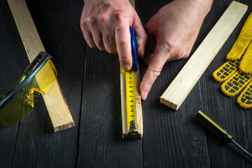 Carpenter or woodworker uses a construction tape to measure the length of a piece of wood. Hands of the master close-up at work. Working environment in a carpentry workshop