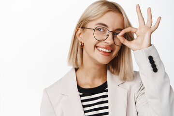 Portrait of businesswoman in glasses smiling, showing okay, zero gesture and looking happy, standing over white background