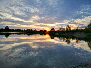 sunset on the lake with reflection. In the horizon row of trees.