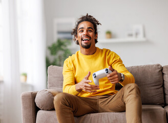 Young positive happy african american guy with wireless gamepad playing video game at home