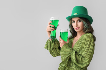 Stylish young woman dressed for St. Patrick's Day party and with glasses of green beer on light...