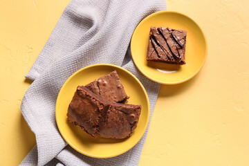 Plates with pieces of tasty chocolate brownie on yellow background