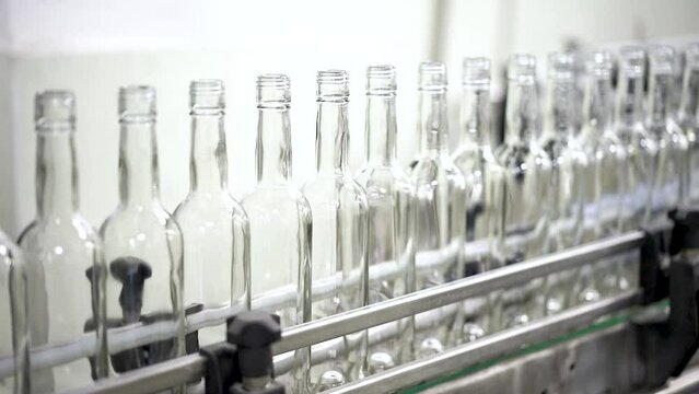 Technological line for bottling of alcohol. Empty bottles in a line in factory. Bottles stoping on Conveyor at distillery.
