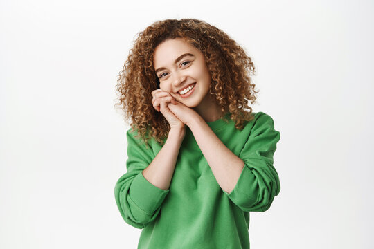 Cute smiling curly woman looking with delight and happiness, gazing tenderly, fascinated by smth, standing over white background