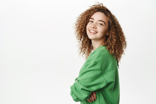 Portrait of modern happy curly girl with white smile, cheerful face expression, standing in green clothes against white background, isolated