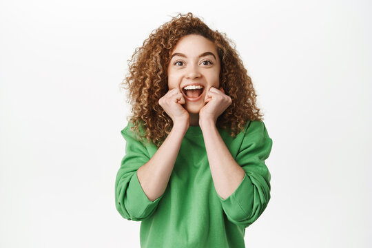 Image of amazed curly woman laughing and smiling with excitement, looking with astonished face, triumphing, standing over white background