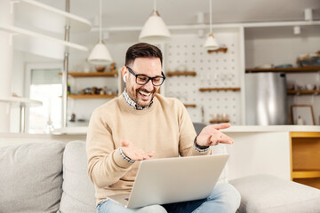 A happy man sitting at his cozy home and having video call on the laptop. A man is laughing and looking at the laptop.