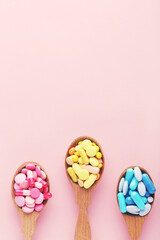 Fototapeta na wymiar Colorful pills in wooden spoons on pink background