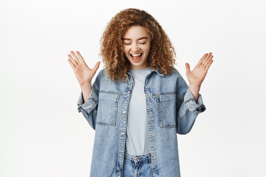 Image of excited and surprised curly woman, looking down and gasping amazed, found smth below, standing over white background