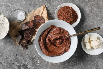 Bowl with fresh dough and ingredients for preparing chocolate brownie on grey background