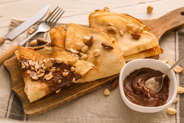 Board of tasty thin pancakes with chocolate paste and nuts on table