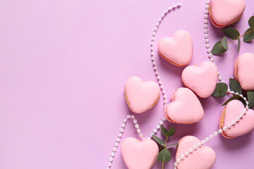 Tasty heart-shaped macaroons with beads and branches on purple background