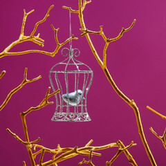 little bird closed in the silver birdcage hanging on a  golden branches on purple color  background. Freedom concept