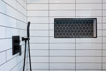 Detail of walk-in shower white subway tile, black hexagon tile inset, and black faucet hardware.