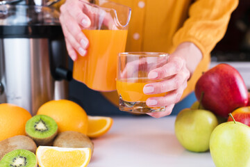 Woman's hands pour freshly squeezed fruit juice into a glass. Natural and healthy juices at home. Close-up. Selective focus.