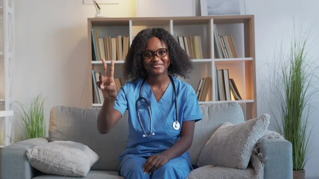Two vaccinations. Covid booster. Doctor advice. Joyful woman nurse showing 2 fingers gesture recommending double shot dose treatment on couch at clinic.