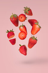 Creative composition with flying ripe strawberries on a bright pink background.