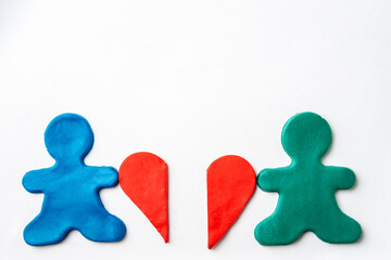 Little men made of blue and green plasticine hold in their hands halves of a red plasticine heart on a white background