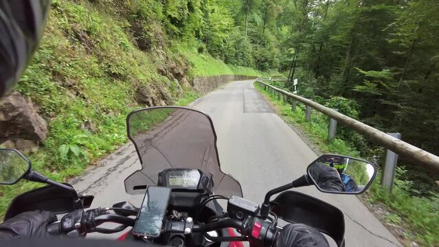 POV Biker rides a motorcycle on scenic mountain road in Liechtenstein. Steering wheel view. Motorcyclist on Motorbike goes by narrow alpine road among the mountain forest and cliffs. First-person view