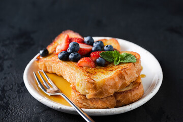 French toast with berries and honey over black background