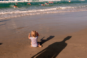 child on the beach watching paddlers in ocean