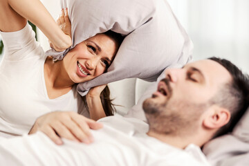 A woman with pillow covering her ears because of her husband's snoring.