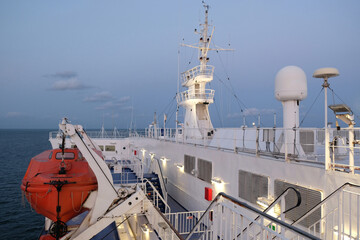 Deck of large passenger ship. Red lifeboat hangs on deck. Communications equipment with sonar,...