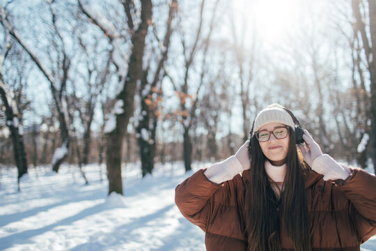 Young woman listening music on headphones on winter day, copy space