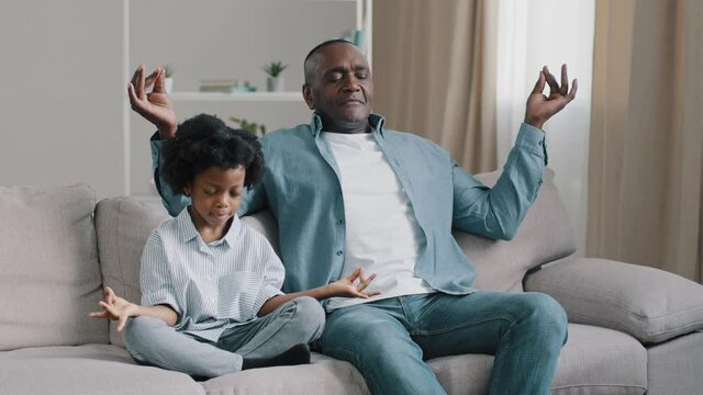 African american father and child sitting on sofa with closed eyes mature dad teaches little daughter to meditate manage emotion calm down do yoga relaxing kid girl sits in lotus position meditation
