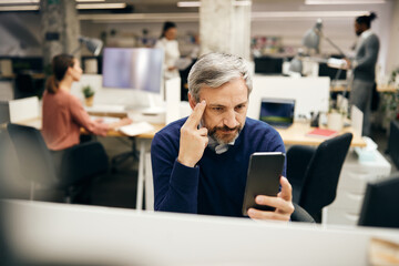 Pensive businessman reads text message on cell phone while working at his office desk.