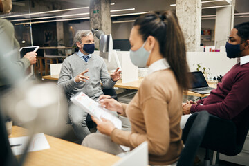 Male CEO talks to multiracial business team while having meeting in the office during coronavirus pandemic.