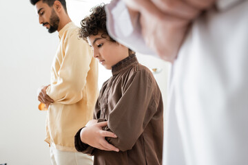 Muslim boy praying near father and blurred granddad at home.