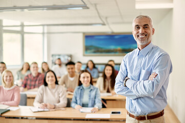 Portrait of happy mature teacher with crossed arms at university classroom.