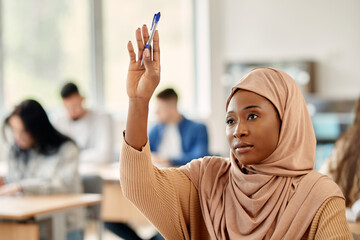 Muslim university student raises her hand to answer question while attending a class at lecture...
