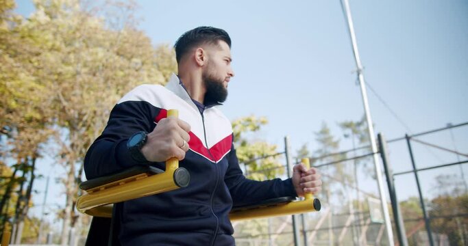 Muscular man doing push ups exercises on parallel bars, ABS, workout outdoors