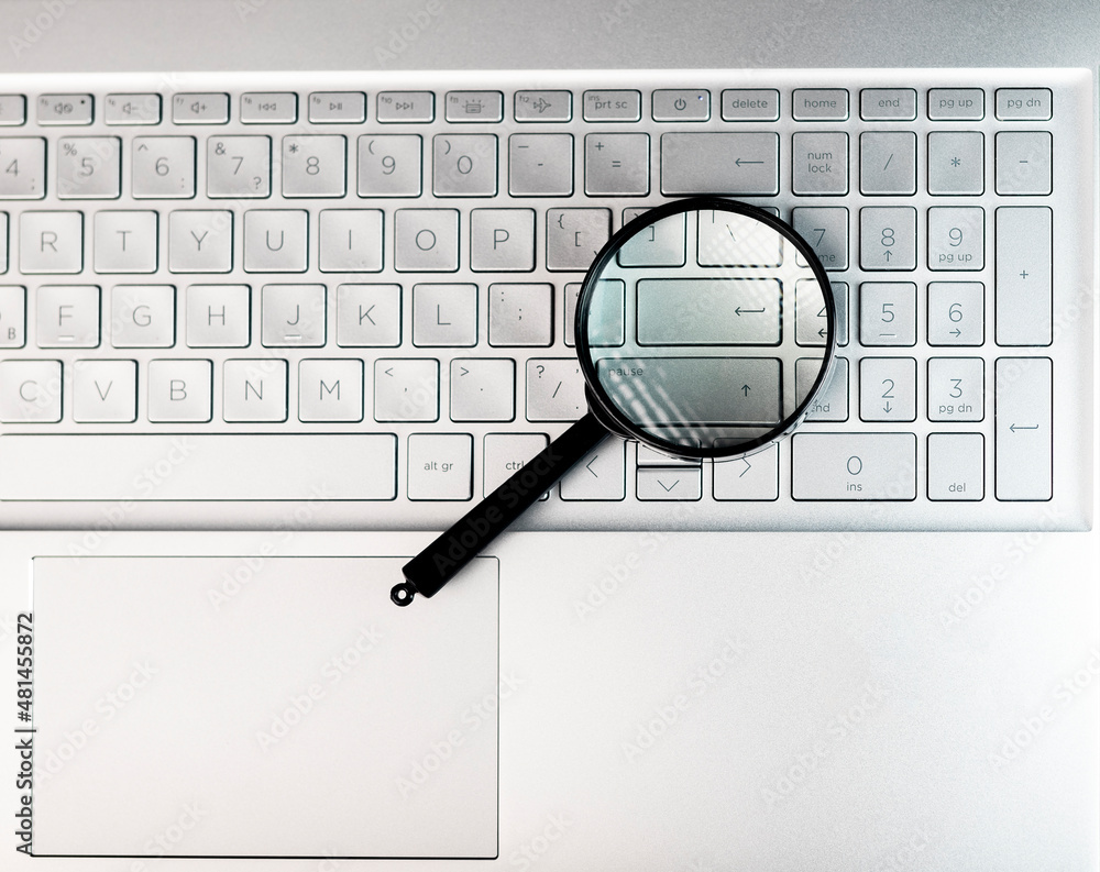 Poster laptops keyboard through magnifying glass. internet search and keywording concept.