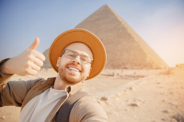 Happy tourist man in hat take selfie photo background pyramid of Egyptian Giza sunset, Cairo, Egypt