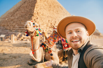 Travel selfie photo tourist man in hat with camel background pyramid of Egyptian Giza, sunset...