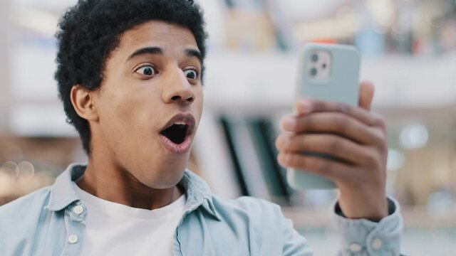 African american surprised shocked amazed man user guy teenager looking at mobile phone opens mouth in surprise delight winning victory discount offer reads shocking news online in smartphone messages