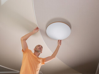 A man in the kitchen fixes a round LED lamp on the ceiling.