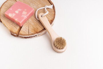 Fototapeta na wymiar Wooden brush for facial or body massage and pink soap on wooden background. Space for text