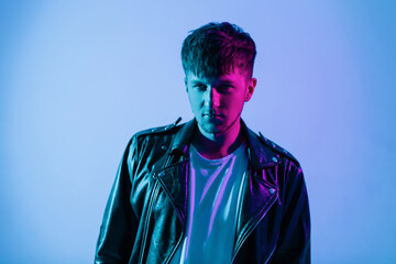 Brutal handsome man model with hairstyle in fashionable black leather jacket with colorful neon and pink light in the studio